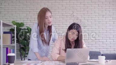 亚洲妇女在她们的小企业的办公室里一起工作，坐着看报告或文件，面带笑容。